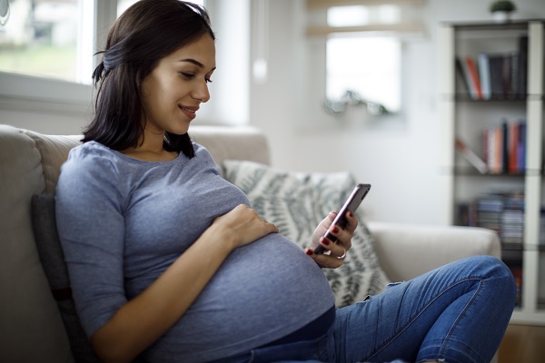 Smiling pregnant woman using mobile phone at home